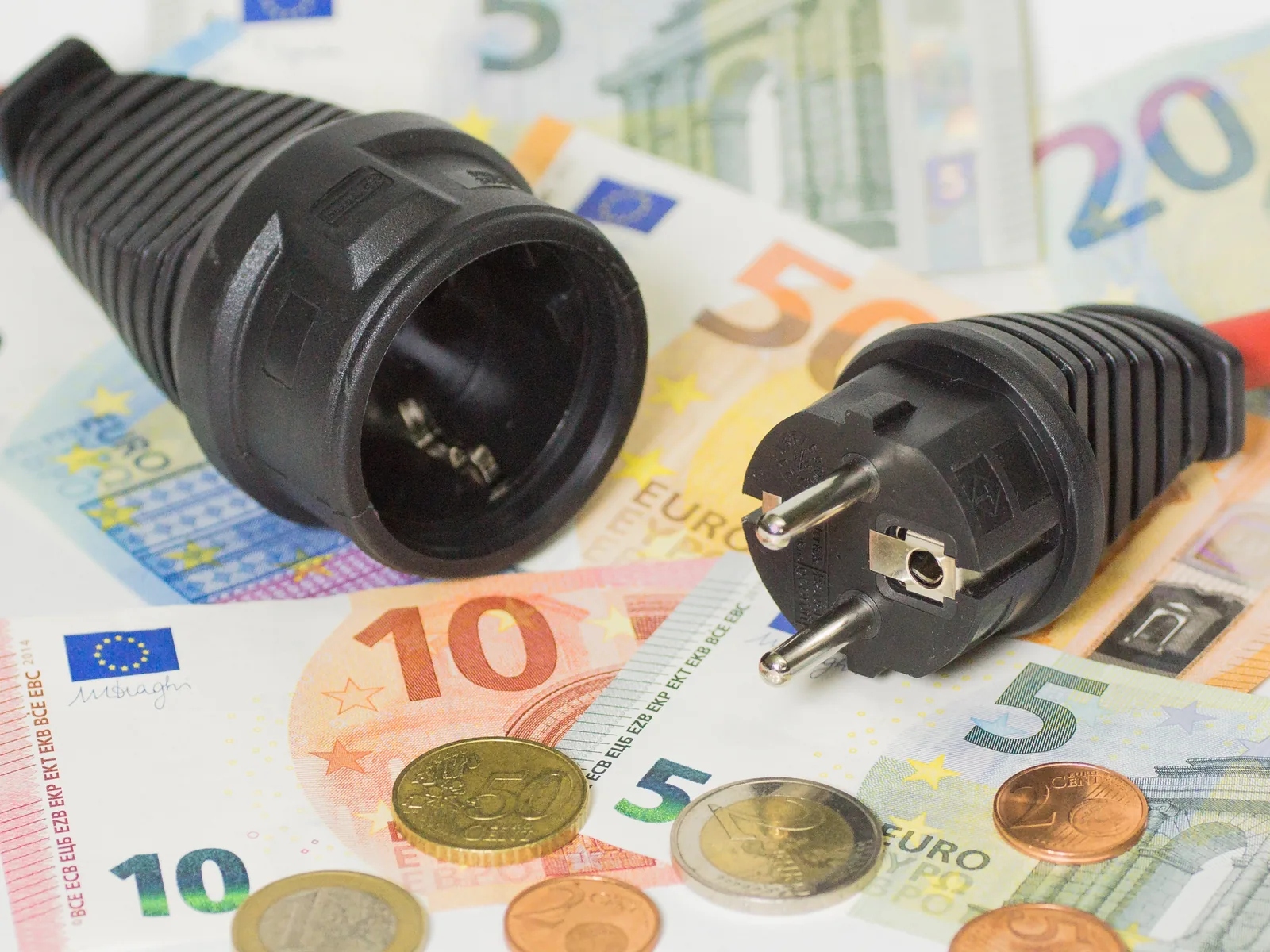 Una spina e una presa elettrica appoggiate su banconote e monete in euro